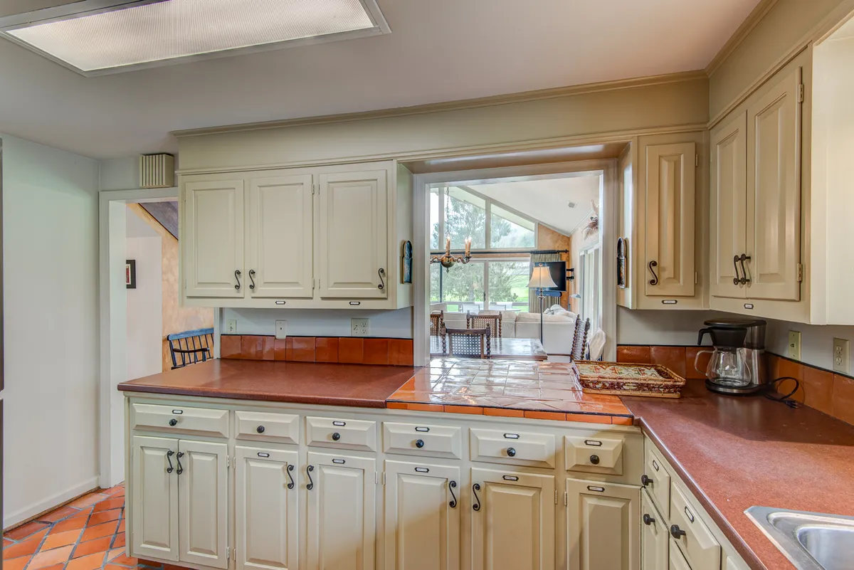 A spacious, modern kitchen featuring a central island, abundant cabinetry, and a view through the window. The setup is ideal for cooking, entertaining, and family gatherings, with open sightlines to the surrounding living spaces.