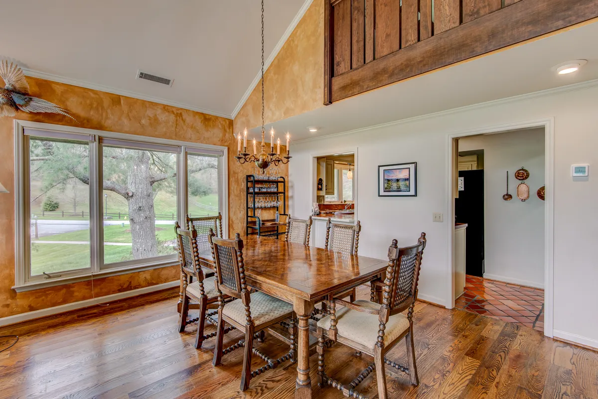 A rustic dining area with a large table, elegant chandelier, and big windows that flood the space with natural light. The setting is cozy and welcoming, ideal for family dinners, entertaining guests, or festive gatherings.