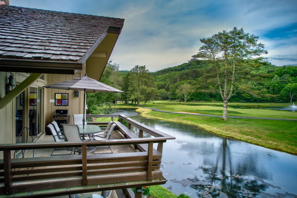 A serene exterior scene showcasing a balcony overlooking a water feature, surrounded by lush greenery and framed by majestic mountains. The mood is tranquil, inviting relaxation, nature walks, and outdoor adventures.
