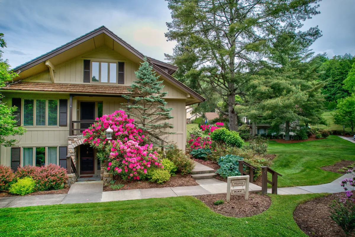 This exterior image showcases a charming front porch surrounded by vibrant flowers and a manicured lawn. The welcoming outdoor seating area faces lush greenery, suggesting a tranquil spot for morning coffee or sunset views.