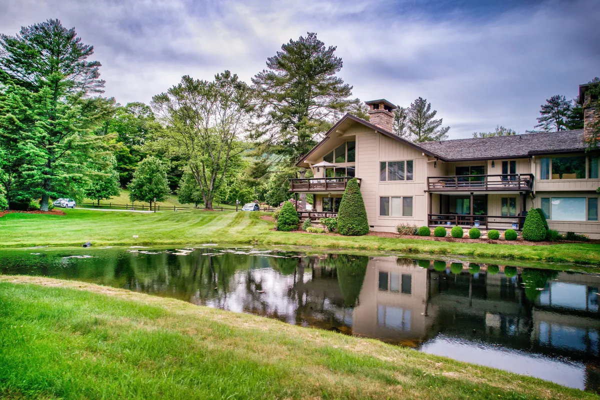 A calm view of the community structure nestled beside a reflective pond and surrounded by mature trees. The area exudes peace and offers a glimpse of the maintained, inviting outdoor spaces available for residents.