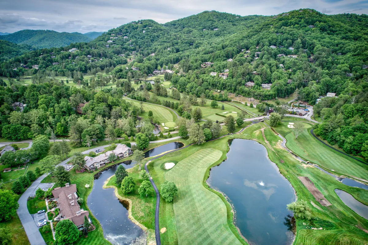 A wide, peaceful view overlooking a golf course, sparkling lakes, rolling hills, and nearby residential properties. The landscape is open and expansive, suggesting ample opportunities for walking, hiking, and enjoying nature’s tranquility.