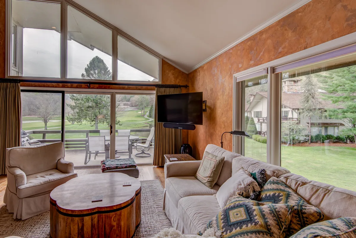 A bright, inviting interior living space with large windows framing sweeping landscape views. Comfortable seating faces the windows, creating a perfect spot for couples to relax while soaking in the serene scenery.
