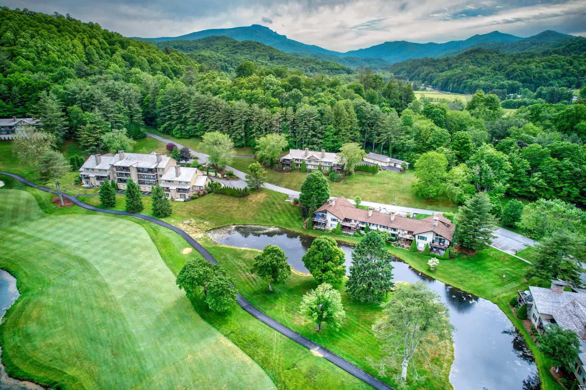 A peaceful scene of a green golf course alongside a tranquil pond, with mountains rising in the background and spacious accommodations nearby. The setting is ideal for quiet walks, relaxation, and enjoying mountain sunsets.